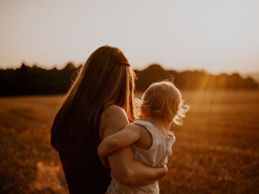Mom holding daughter in sunset
